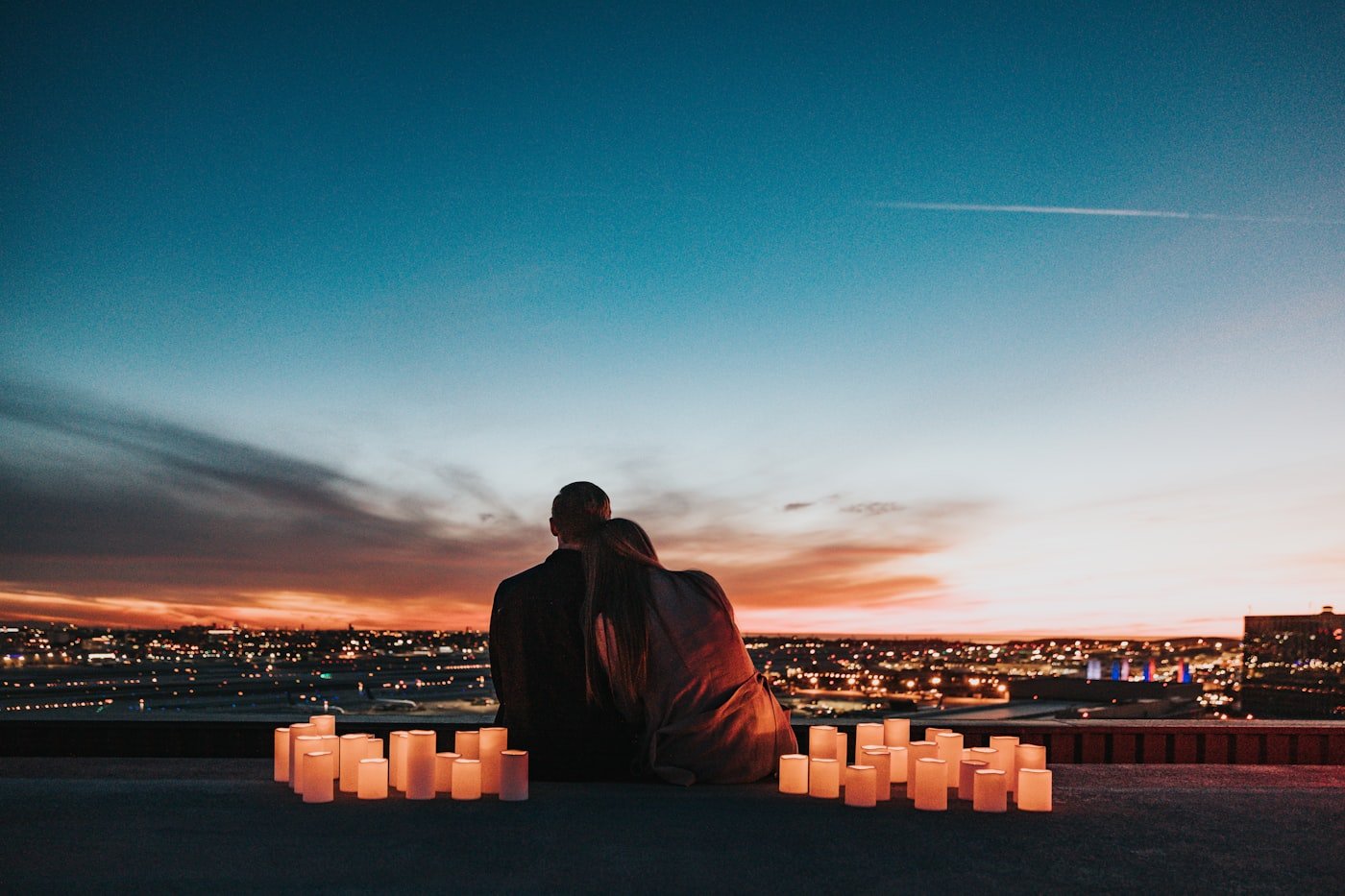 Couple sitting behind glowing candles overlooking a city skyline at night during a romantic city getaway